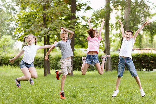 Fyra barn som lekfullt hoppar i luften med en grönskande bakgrund.
