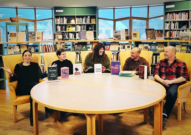 Fem bibliotekarier sitter samlade kring ett bord. På bordet står en samling böcker. Alla ser glada ut.