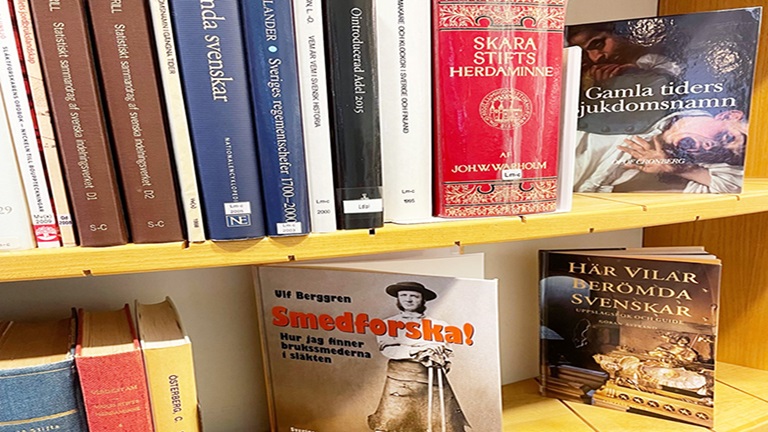 En närbild på en träfärgad bokhylla med litteratur om släktforskning uppställd.