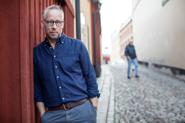 Bilden visar Po Tidholm som lutar sig mot en röd husvägg. Foto av Peter Hoelstad