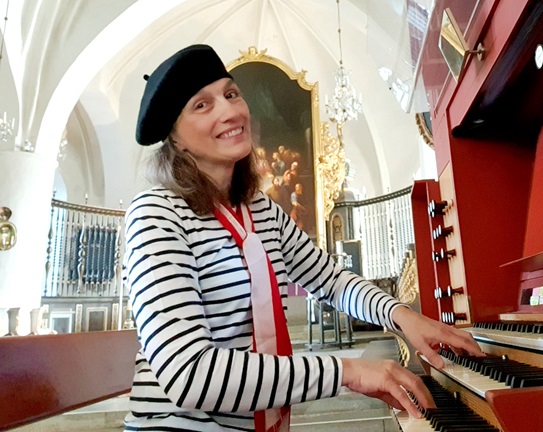 Organist Inger Dalene sitter vid kyrkorgeln i S:t Nicolai kyrka iklädd basker. 
