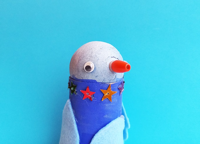 En hemmagjord pingvin i papper med stjärnor kring halsen. Pingvinen är blå och vit med röd näbb. Bakgrunden är isblå.