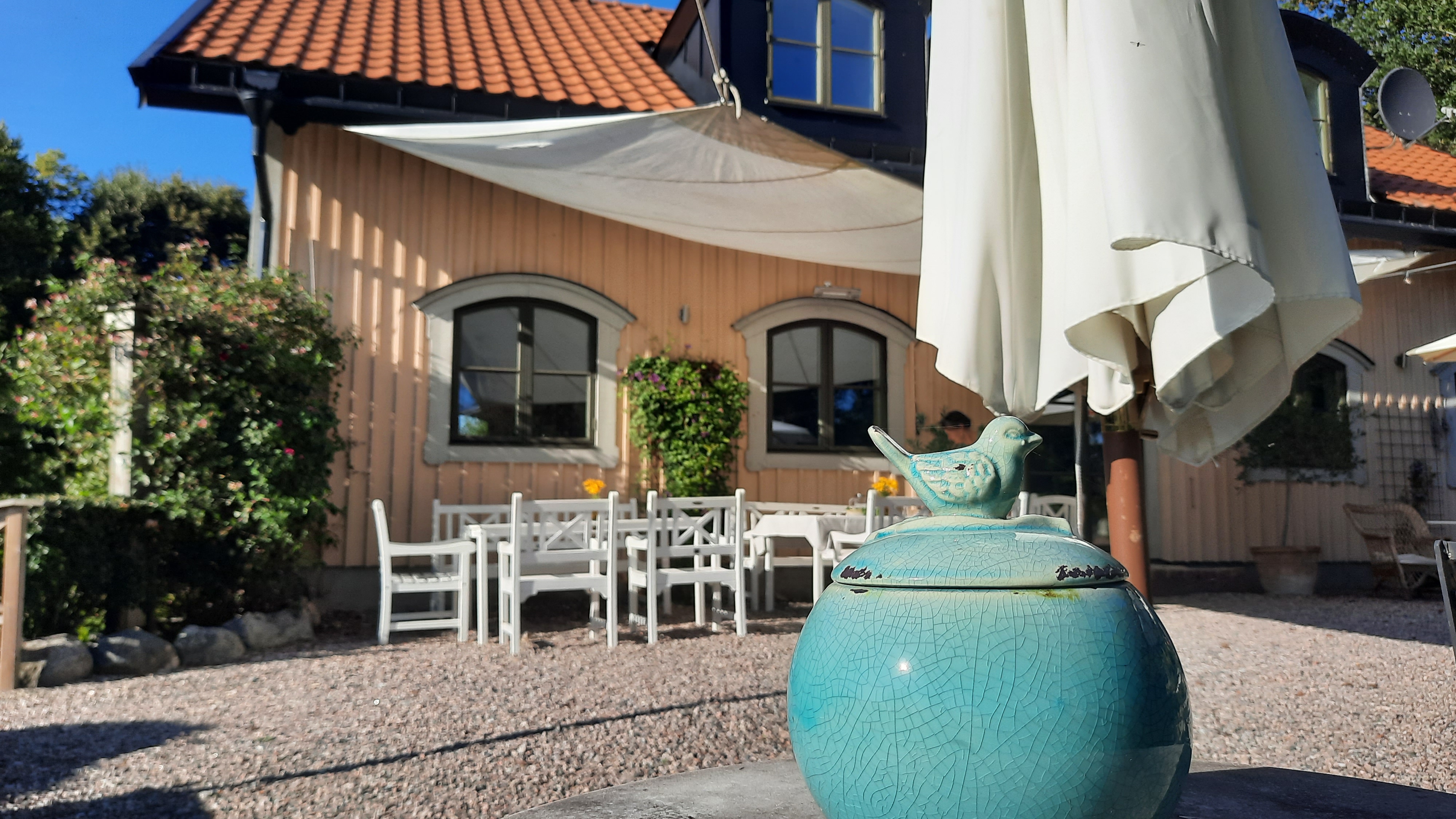 Gul byggnad med vitt parasoll utanför. I förgrunden syns en blå porslinsskål på ett bord.