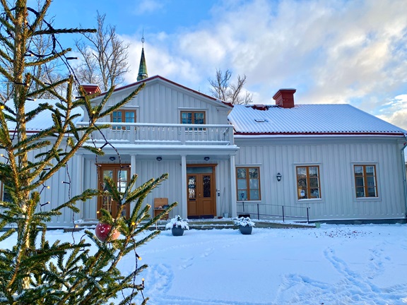Prosten Pihls gård i vinterskrud med en julgran i förgrunden.