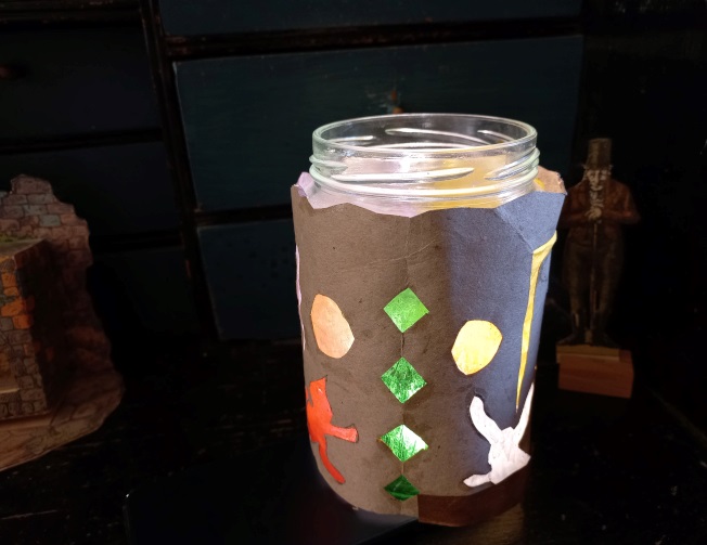 En glasburk pyntad med brunt papper och prickar i olika färger. 