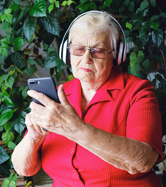 En gammal kvinna i röd skjorta tittar koncentrerat på mobilen hon har i händerna.