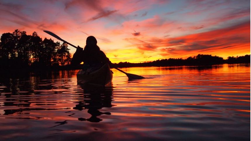 En person som paddlar kajak i solnedgång. Himlen är röd och gul.
