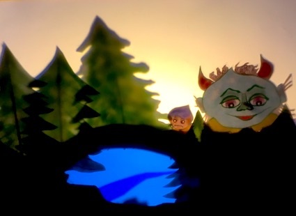 Två troll bredvid en liten sjö. I bakgrunden ser man solen gå ned bakom några granar.