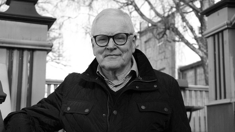 P-O. Äldre gråhårig man med svarta glasögon och vinterjacka,  framför NK-villan