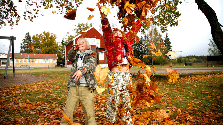 Två barn kastar färgglada höstlöv i luften.