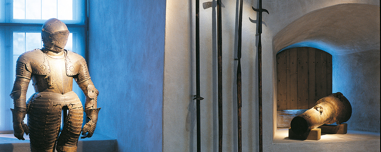 En gammal rustning, kanon och fyra verktyg står på en utställning.