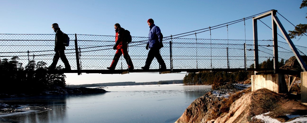 Tre personer går över en hängbro i vintertid.