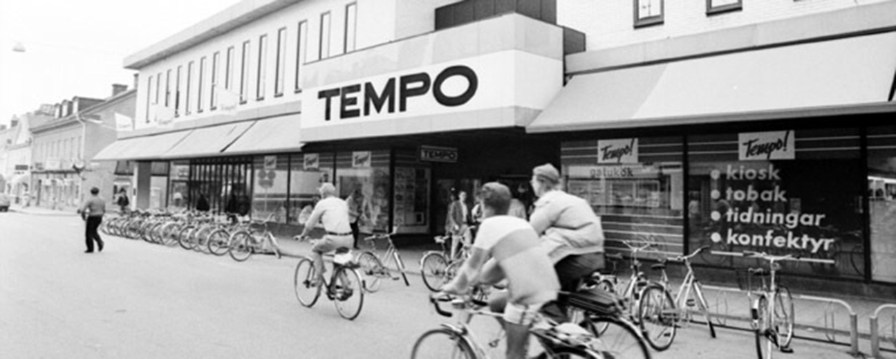 En svartvit bild på en gammal affär i Nyköping, folk som cyklar och går utanför