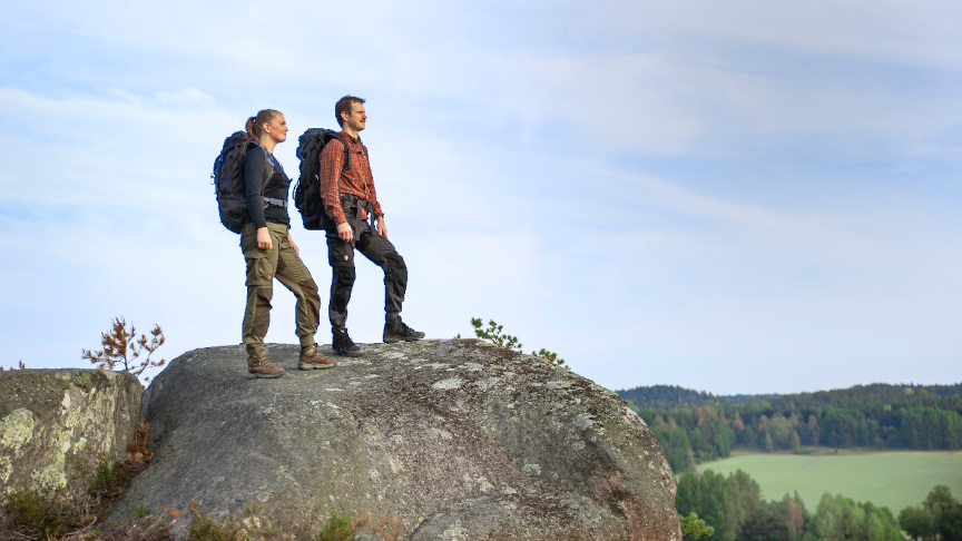 En kvinna och en man står och kollar ut över utsikten på ett berg