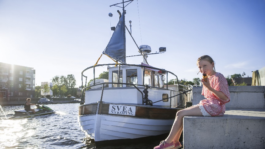 En flicka äter glass framför en båt i Nyköpings hamn.