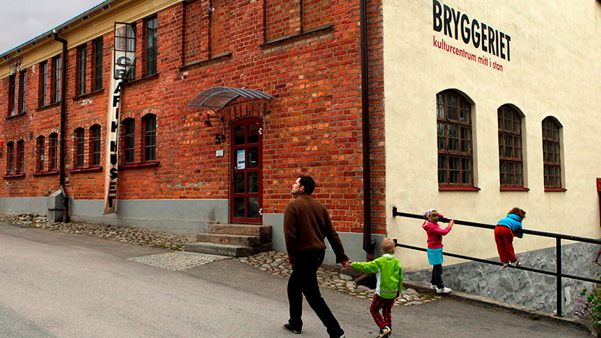En vuxen med tre barn framför den gula och röda tegelbyggnaden i bryggeriområdet.